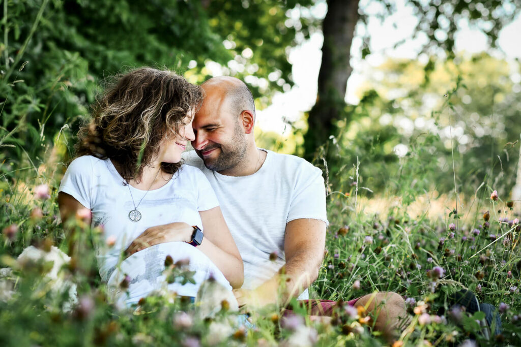 Schwangere Frau mit ihrem Partner sitzen auf einer Wiese. Familienfotografie Wetterau